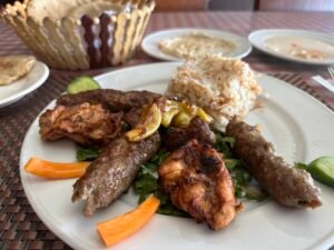 Plate of Egyptian mixed grill with kofta, grilled chicken, rice, greens, carrots, cucumber, and lime