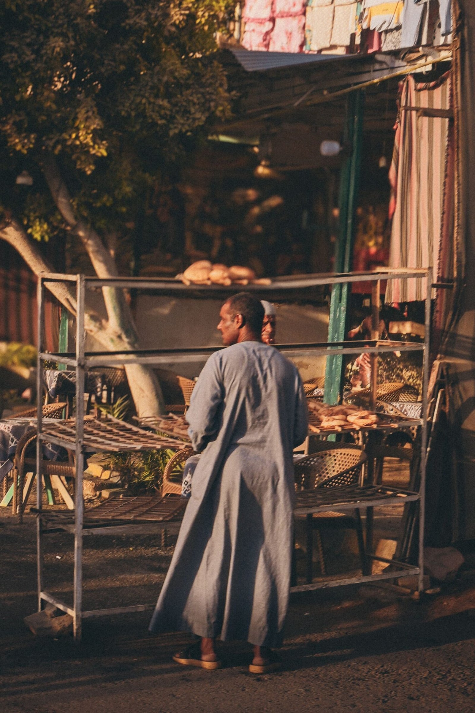 Local street vendor in traditional clothing beside a market stall in Edfu, Egypt
