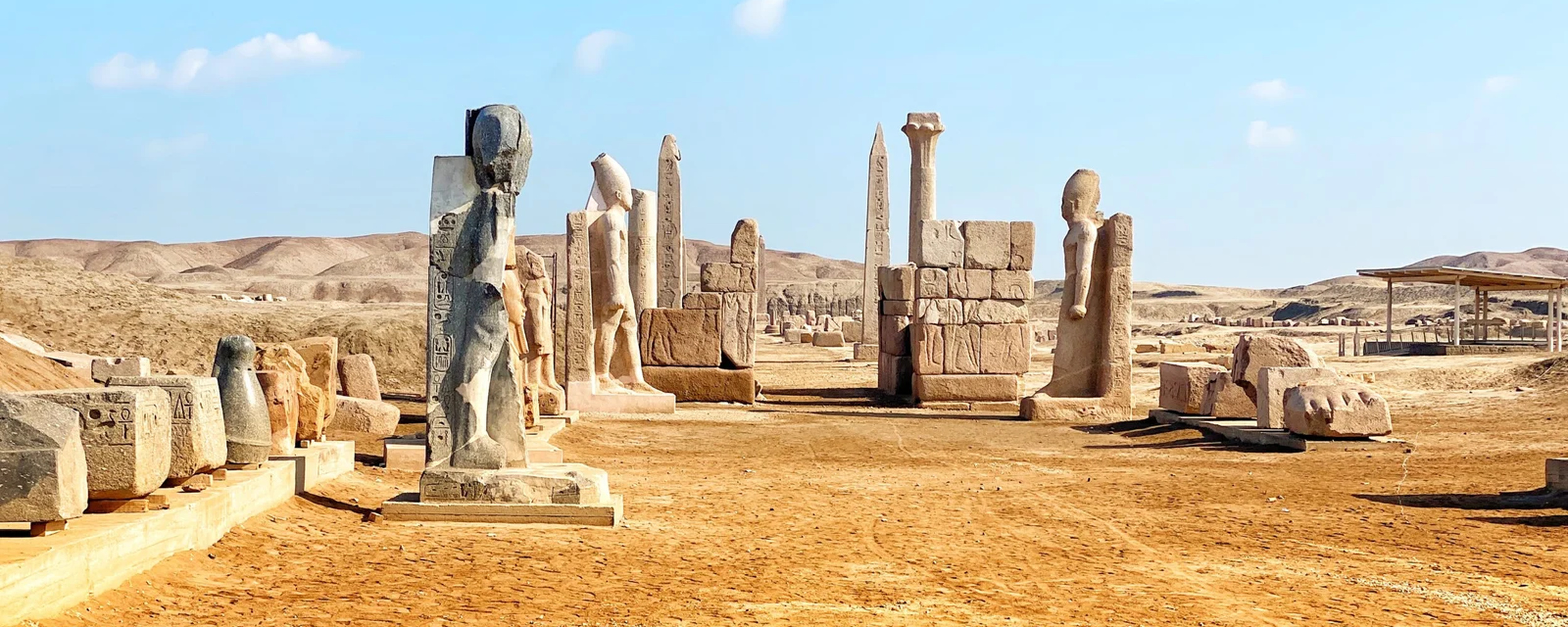Wide 2500×1000 crop of royal statues, inscribed Ramesside obelisks, columns and carved blocks in the Great Temple of Amun at Tanis, Egypt
