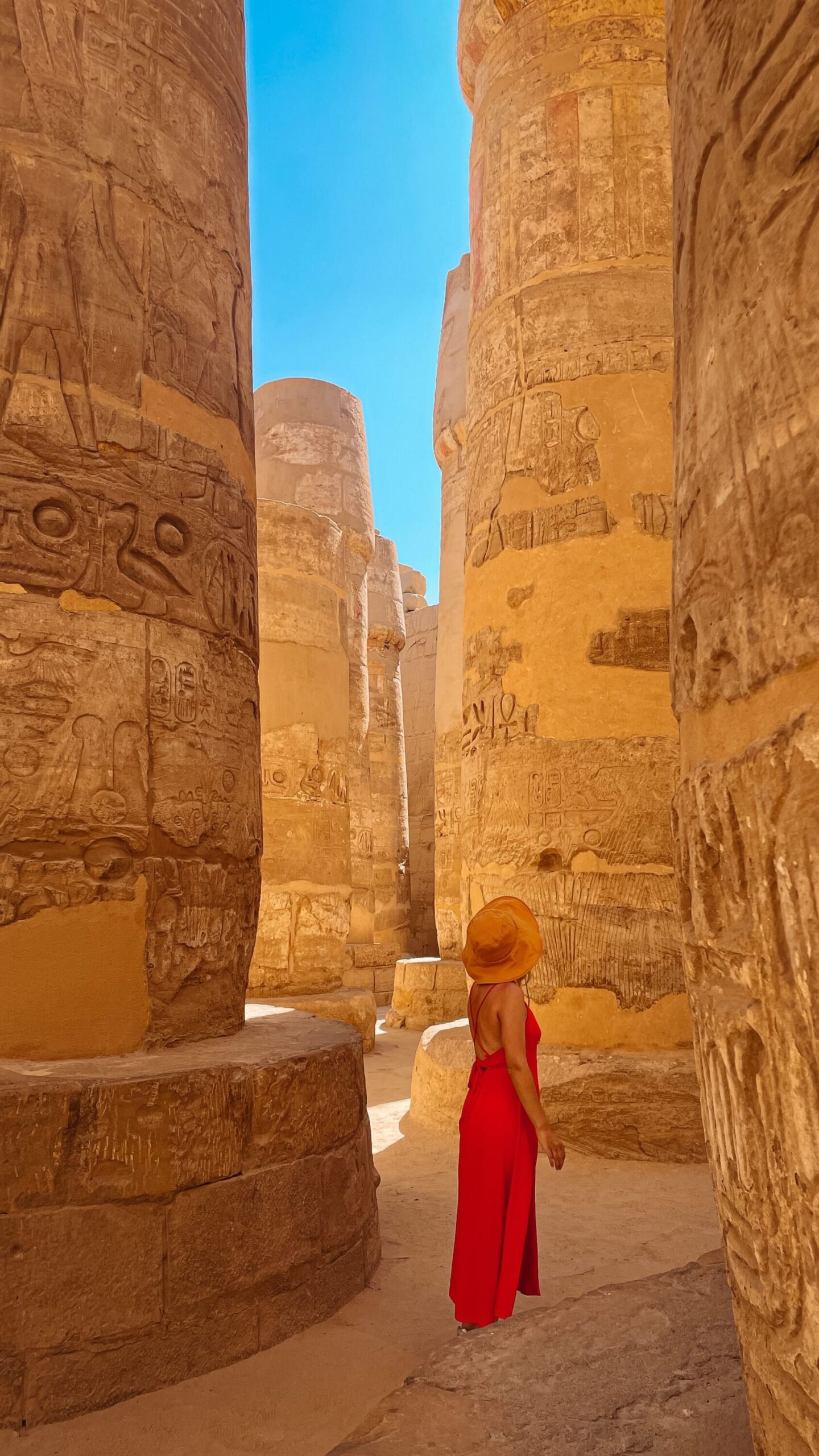 Woman in a sun hat and lightweight dress walking among the massive carved columns of Karnak Temple in Luxor, Egypt